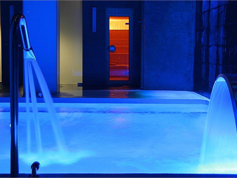 Oświetlony jacuzzi z dyszami wodnymi w niebieskim i pomarańczowym świetle w nowoczesnym wnętrzu.