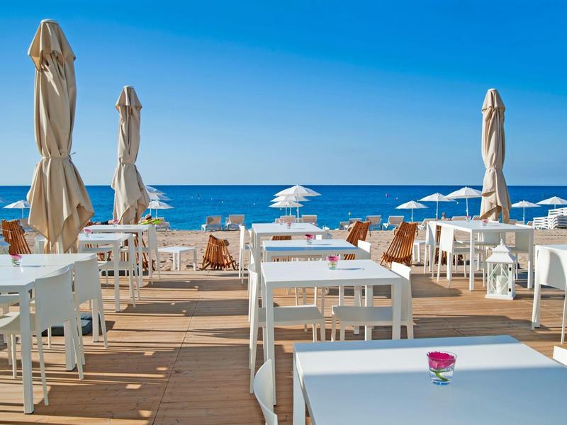 Pusta przestrzeń tarasu z białymi stołami i krzesłami blisko plaży pod niebieskim niebem.