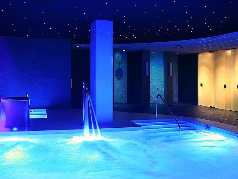 Ogrzewane jacuzzi z schodkami i oświetloną przebieralnią w ciemnej strefie spa.