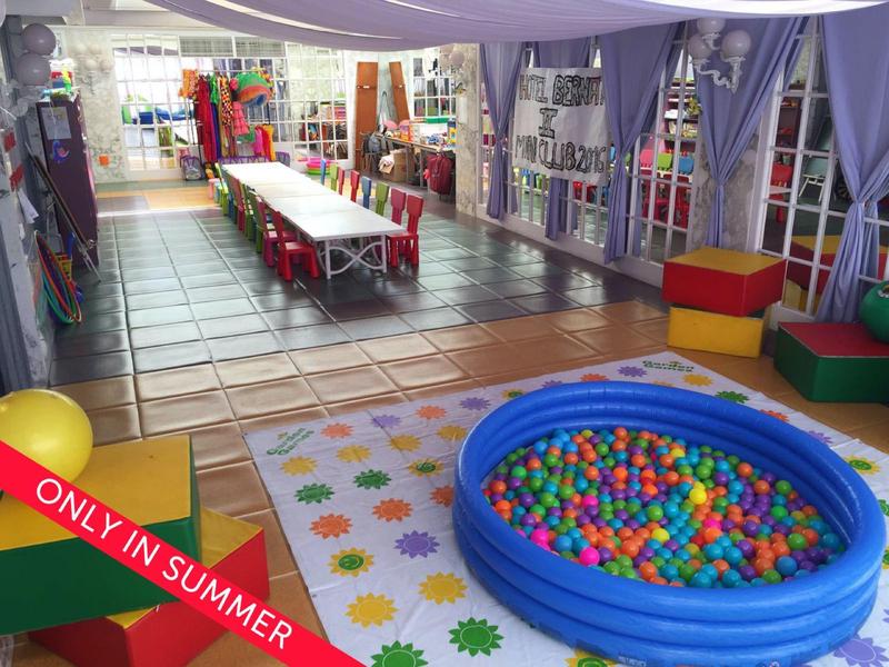 Jasny, kolorowy pokój zabaw z basenem z piłeczkami i długim stołem dla dzieci w obiekcie wypoczynkowym.
