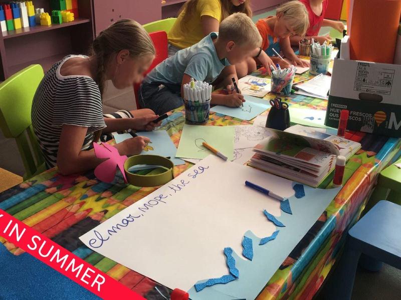 Dzieci siedzą przy stole, rysując i wykonując prace ręczne w kolorowym pomieszczeniu.