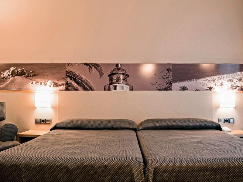 Pokój dwuosobowy z dwoma pojedynczymi łóżkami, szarymi narzutami i lampami ściennymi LED