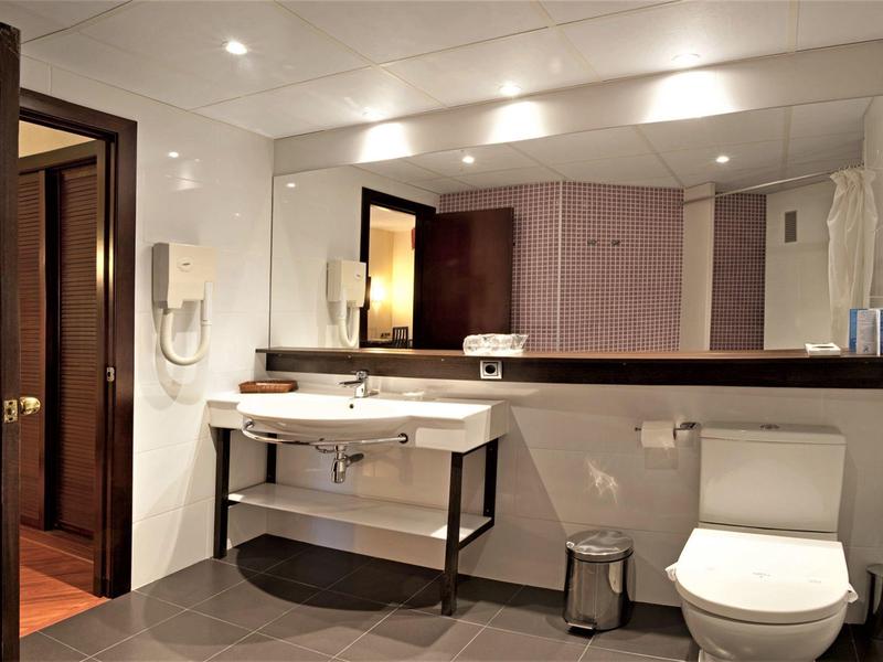 Nowoczesna łazienka hotelowa z dużym lustrem, umywalką, toaletą i oświetleniem sufitowym.