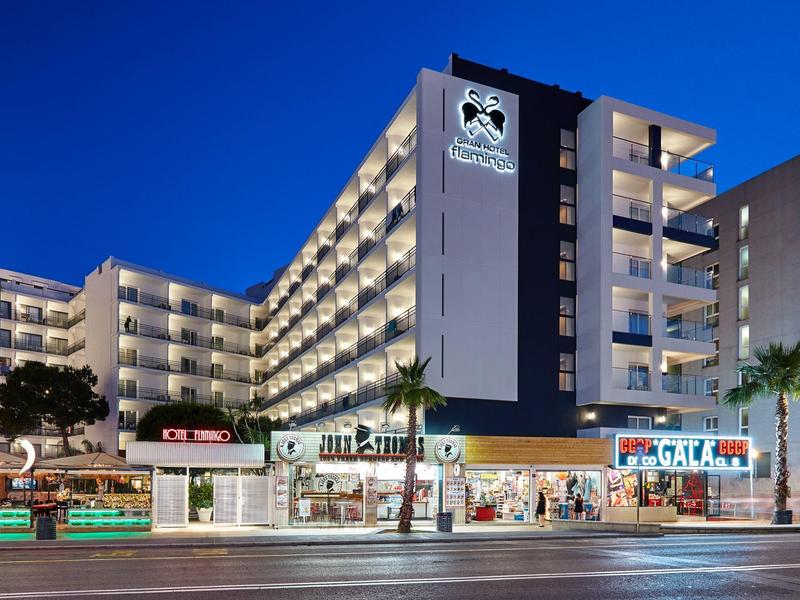 Edificio moderno dell'hotel con balconi illuminati e negozi al piano terra di notte.