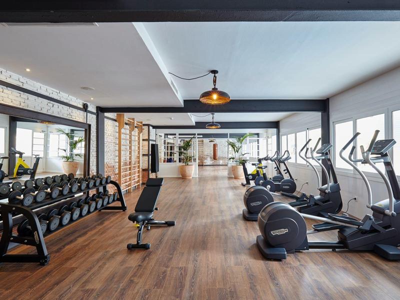 Palestra luminosa con pavimento in legno, attrezzi da palestra e pesi liberi.