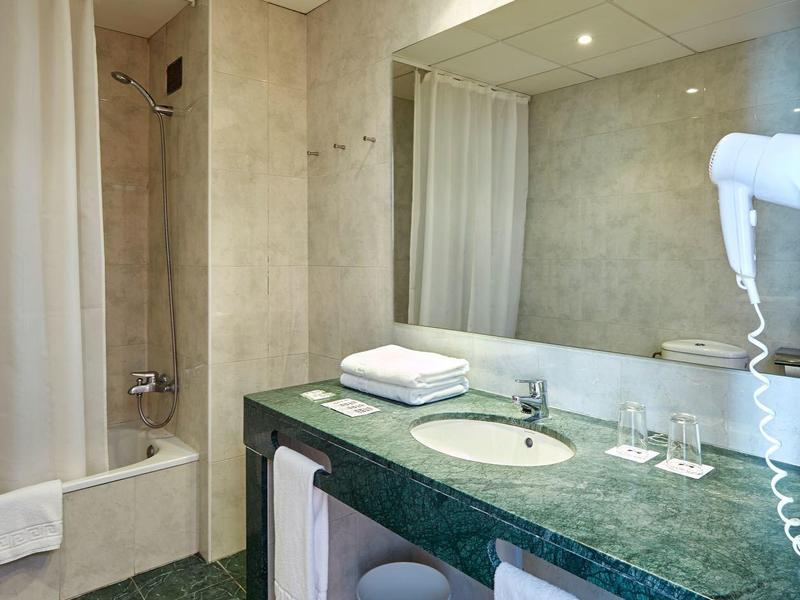 Bagno moderno con piano in marmo verde, grande specchio e vasca con tenda da doccia.