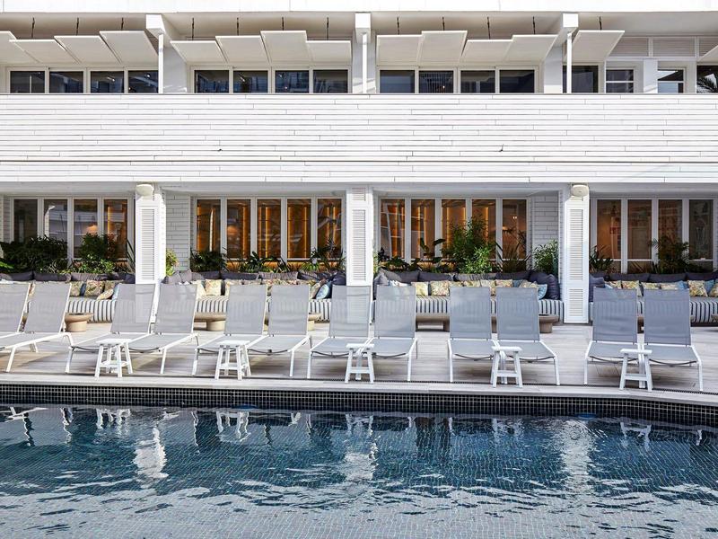 Piscina moderna dell'hotel con lettini bianchi davanti a una fila di edifici bianchi.