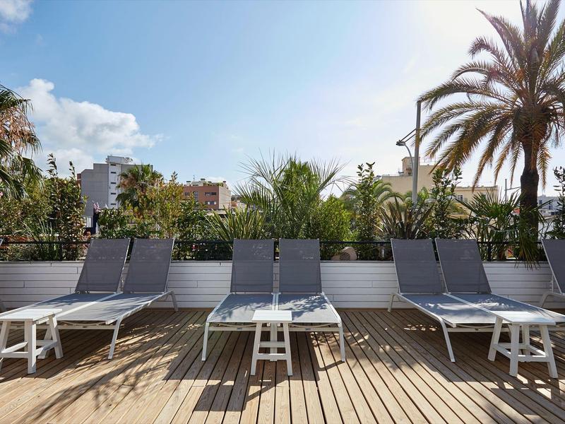 Area esterna con sedie a sdraio e tavoli davanti a palme e piante su una terrazza in legno.