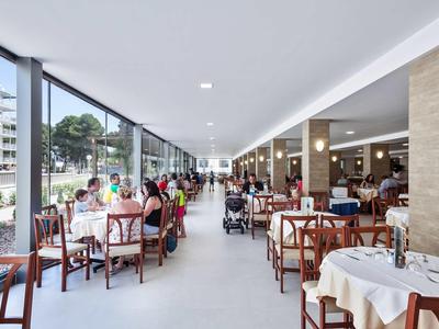 Ristorante luminoso con grandi finestre e numerosi tavoli apparecchiati vicino a una strada cittadina.