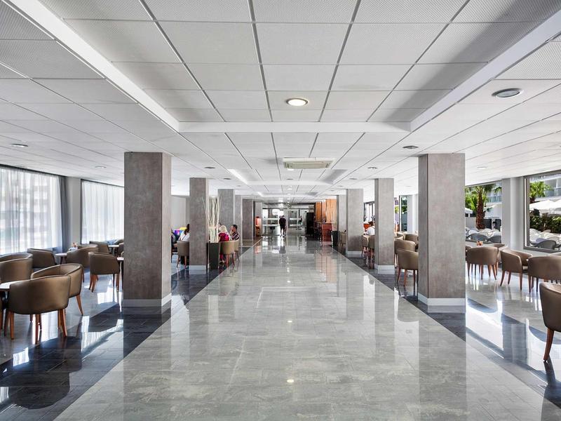 Ampia e luminosa sala ristorante dell'hotel con finestre in vetro, tavoli e sedie lungo un corridoio in marmo.