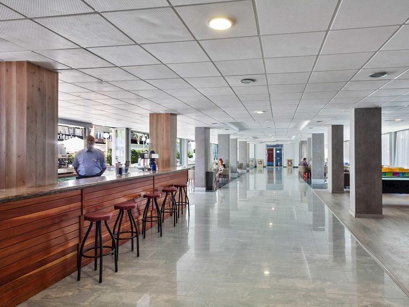 Ampia hall d'albergo luminosa con bancone bar e posti a sedere.