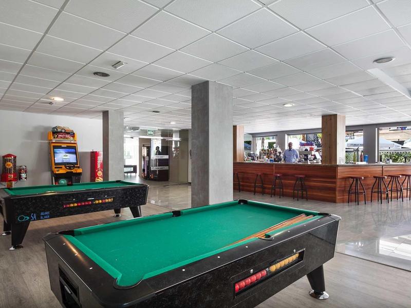 Lounge d'hotel moderna con tavoli da biliardo e area bar con sgabelli.