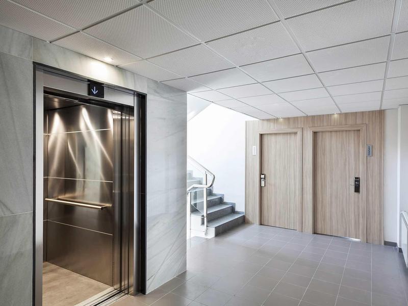 Corridoio d'hotel moderno con ascensore aperto e scala che conduce alle camere.