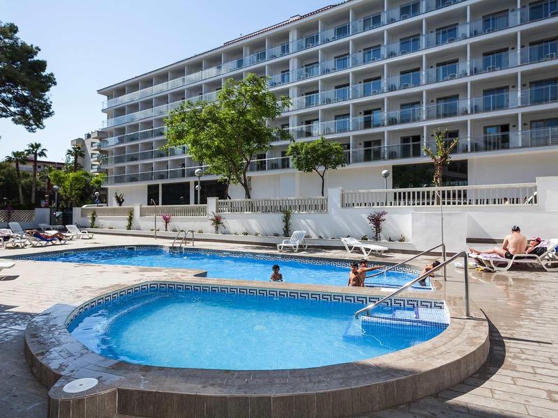 Piscina esterna con vasca idromassaggio davanti a un hotel su più piani con lettini