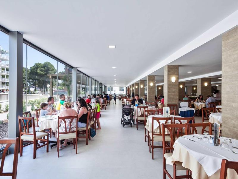 Ristorante luminoso con grandi finestre e numerosi tavoli apparecchiati vicino a una strada cittadina.