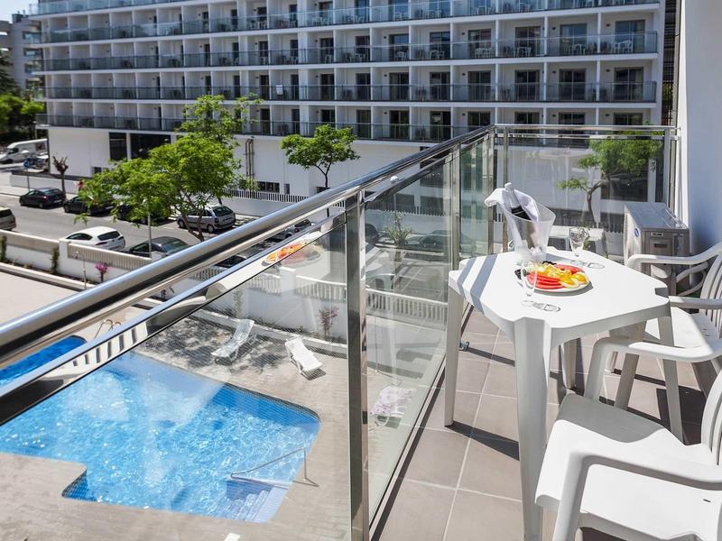Balcone con tavolo bianco e sedie con vista sulla piscina di un hotel.