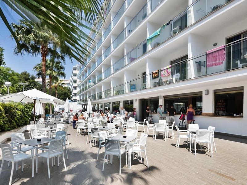 Terrazza dell'hotel moderna con tavoli e sedie bianchi, ombrelloni e palme.