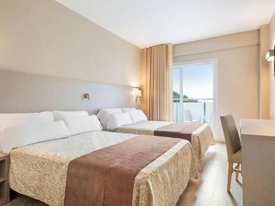 Bright hotel room with two beds, beige walls, and a window with a view.