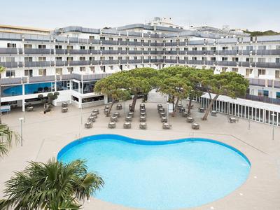 Hotel with a kidney-shaped pool, lounge chairs, and trees in the courtyard.