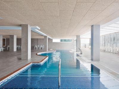 Indoor pool with blue water, lounge chairs, and white ceiling in a bright room.