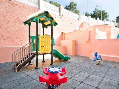 Small playground with slide and spring rider on tiled floor near peach colored walls.