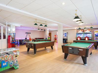 Sala giochi con tavoli da biliardo, flipper e slot machine in uno spazio luminoso.