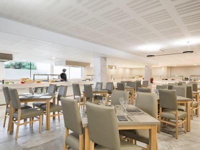 Spacious hotel dining area with tables and gray cushioned chairs arranged neatly.