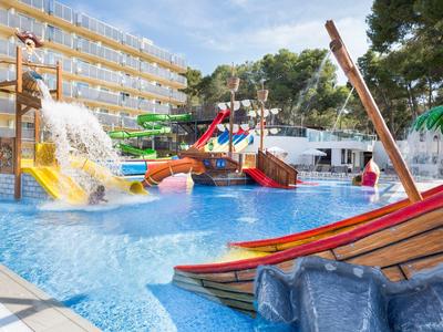 Water park with slides and a splash pool near a hotel building under a blue sky.