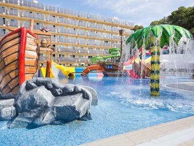 Outdoor water park with slides, a water-spraying palm tree, and pools by a hotel.