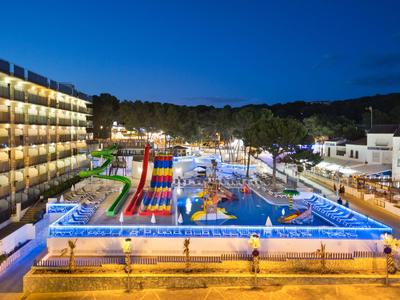 Parco acquatico illuminato con piscina e scivoli accanto a un hotel di notte.