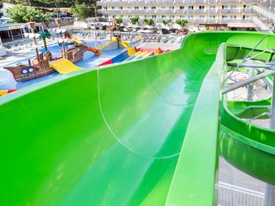 Bright green water slide curving downward near a poolside lounge area.