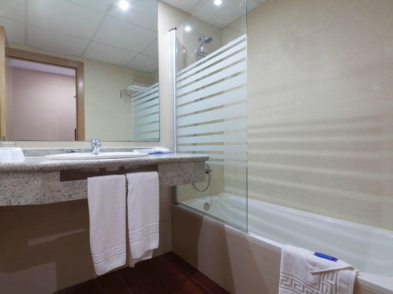 Modern hotel bathroom with bathtub, glass shower screen, and sink with towels.
