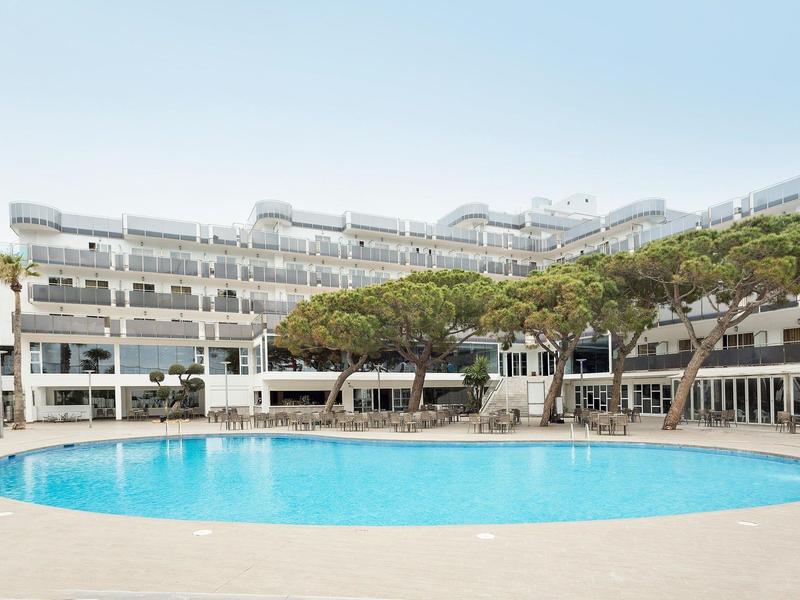 Round swimming pool in front of a modern hotel with trees and balconies.