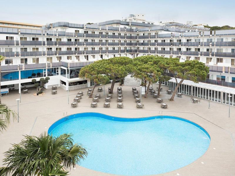 Hotel with a kidney-shaped pool, lounge chairs, and trees in the courtyard.