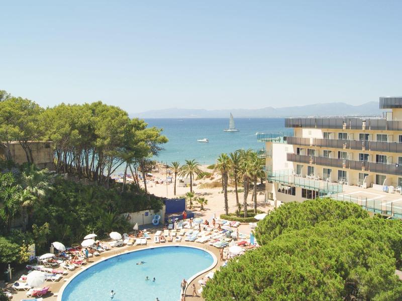Outdoor hotel pool with water slides and pirate ship play area surrounded by sunlit trees.