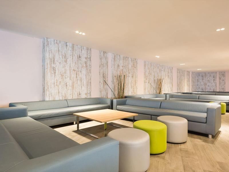 Modern hotel lounge with grey sofas, small tables, and round stools on wooden floor.