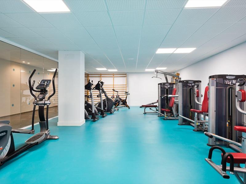 Modern gym with exercise equipment and blue flooring, bright ceiling lights