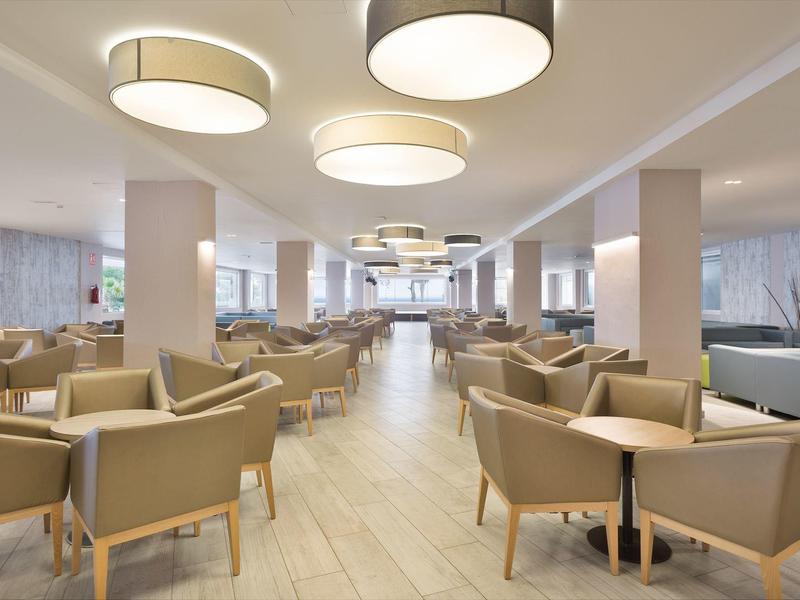Modern hotel lobby with beige armchairs, round tables, and large ceiling lights.