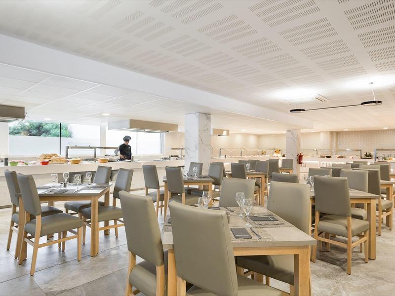 Spacious hotel dining area with tables and gray cushioned chairs arranged neatly.