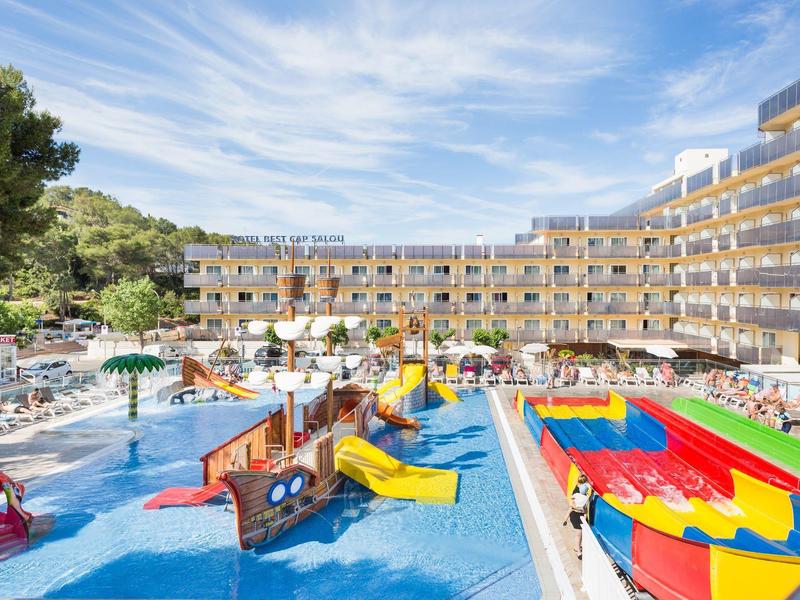 Hotel with large outdoor pool, waterslides, and a play area under blue sky.
