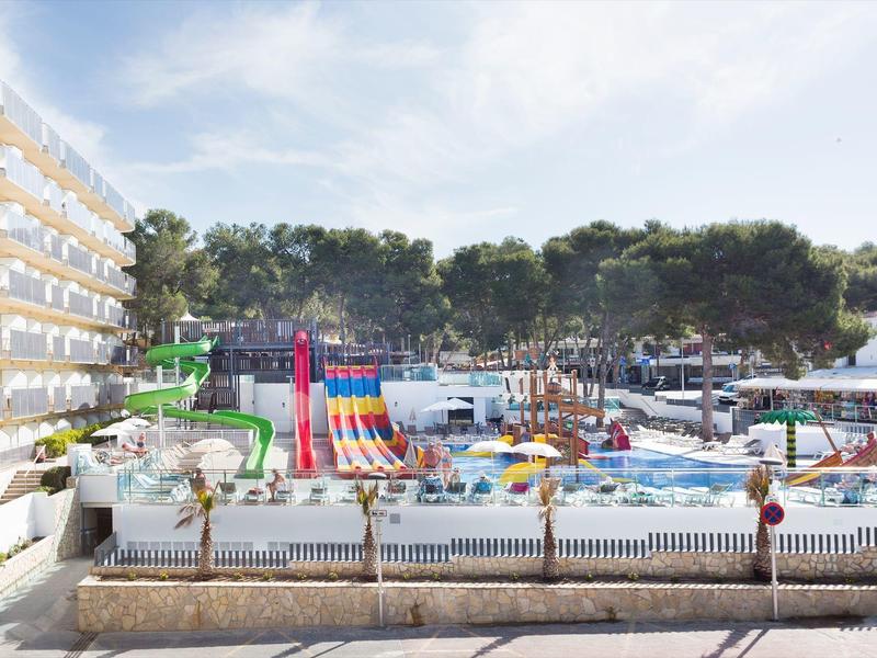 Large outdoor water park with colorful slides and pools next to a hotel under a blue sky.