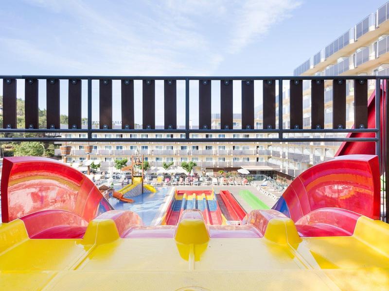 View from the top of colorful water slides at a sunny water park with pools and lounging area.