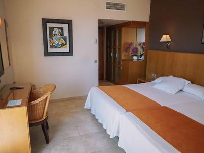 Jasno urządzony pokój hotelowy z łóżkiem podwójnym, biurkiem i krzesłem.