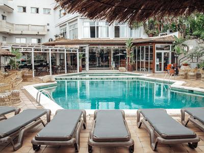 Basen hotelowy z leżakami i zadaszonym tarasem, otoczony wielopiętrowymi budynkami.