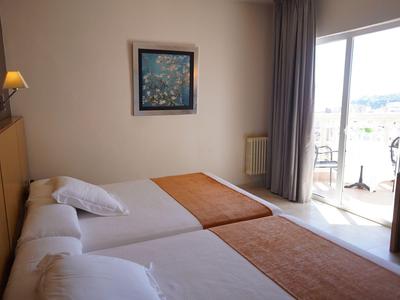Pokój hotelowy z dwoma łóżkami, pomarańczowymi narzutami i balkonem z krzesłami.