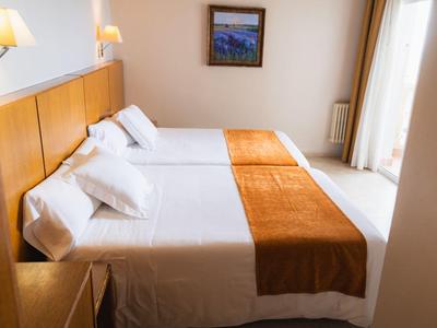 Pokój hotelowy z dwoma pojedynczymi łóżkami, białą pościelą i pomarańczowymi narzutami w nowoczesnym stylu.