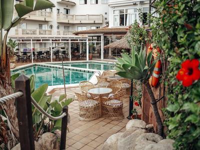 Taras hotelowy z basenem, stołami i krzesłami, otoczony roślinami i dekoracjami kwiatowymi.