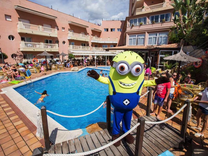 Hotel pool area with guests, chairs, and a person in a Minion costume near the water.