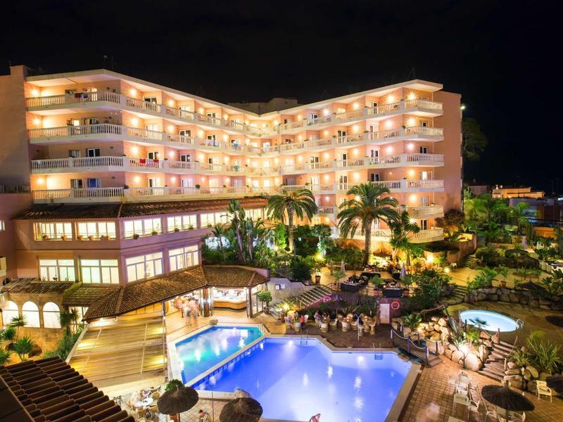 Night view of a lit hotel with swimming pool and palm trees in a tropical setting.