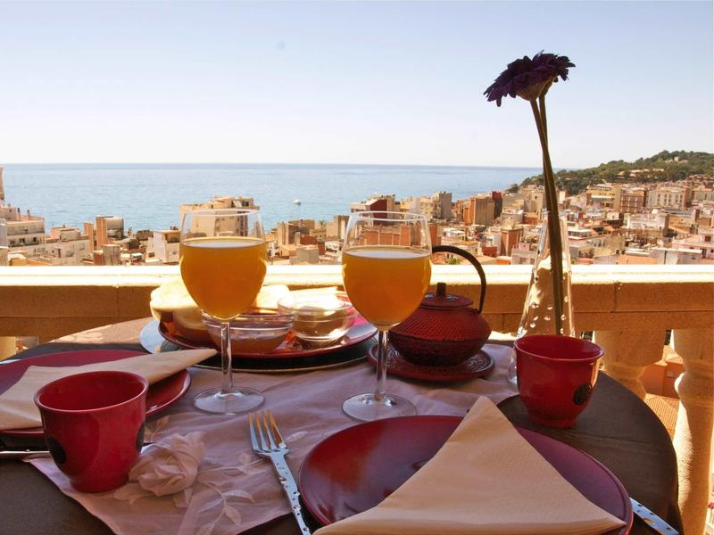 Table set with drinks and a single flower, overlooking a coastal town and sea view.